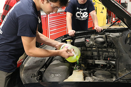 Student pouring liquid into car part