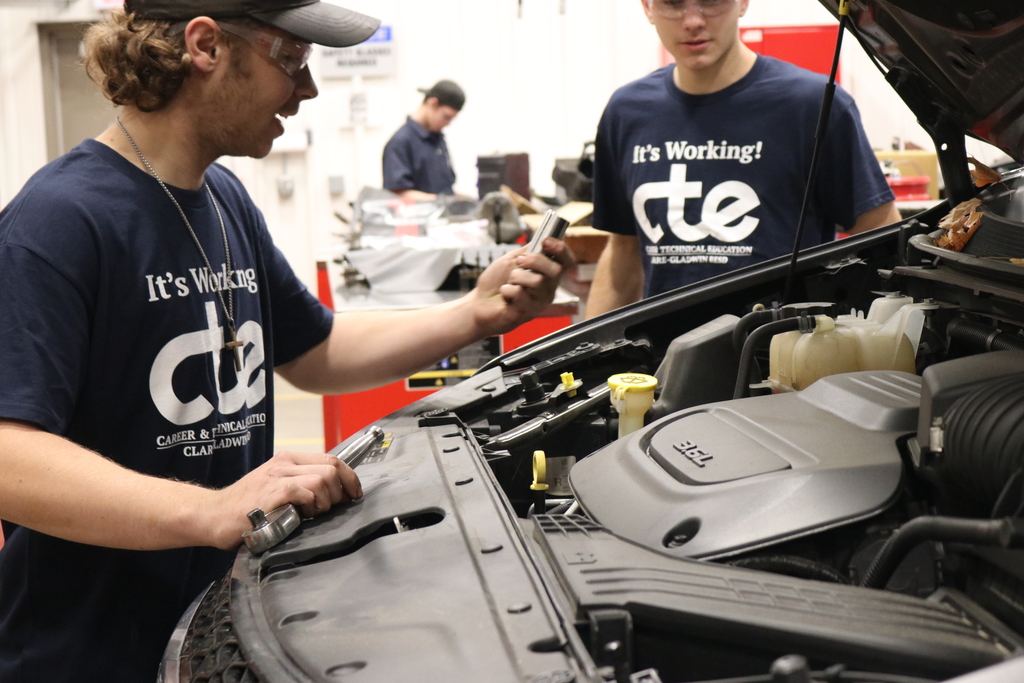 Student holding tools in front of car 