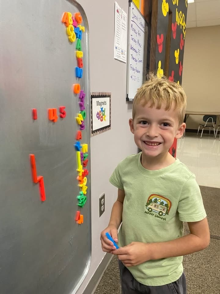 student standing next to magnetic board putting magnets on board