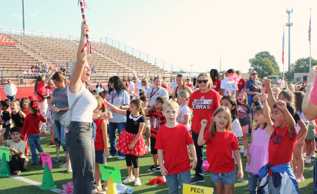 principal holding the spirit stick with students cheering