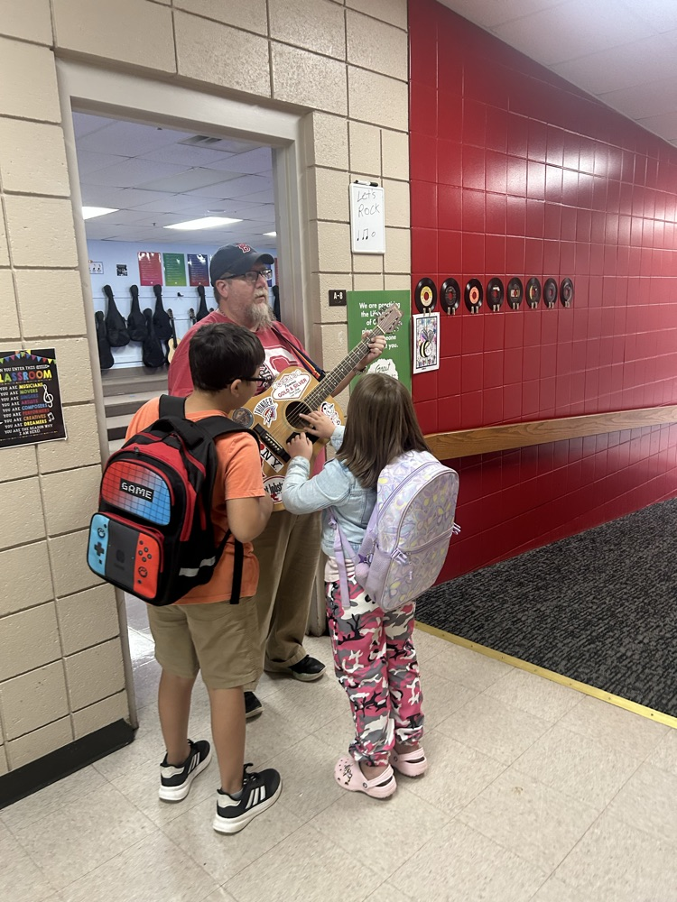Mr. Levesque playing his guitar in the halls after school with students listening.