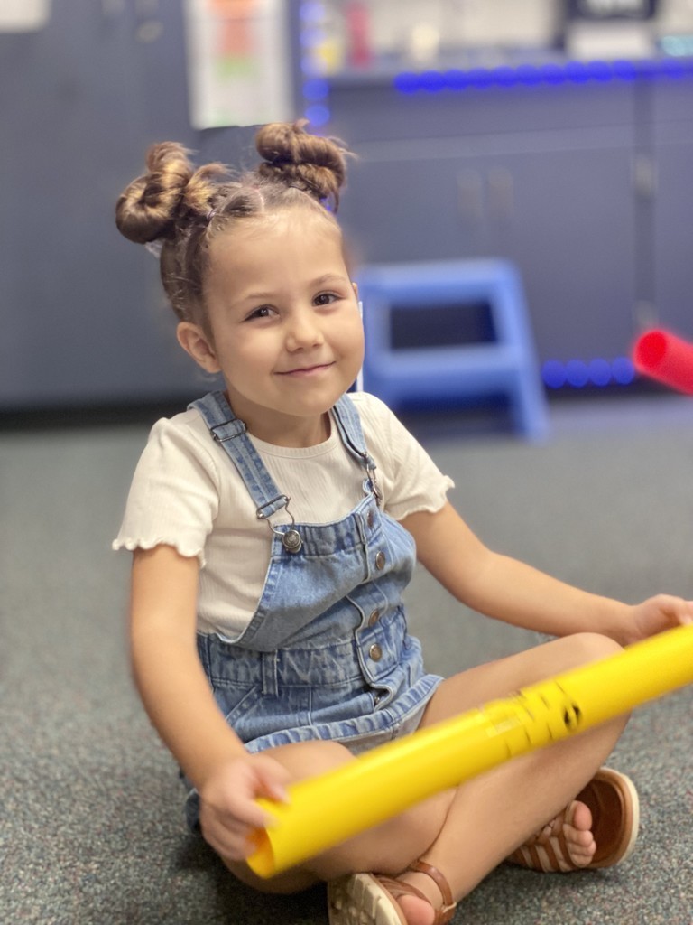 student with pigtails and overalls smiling for a picture