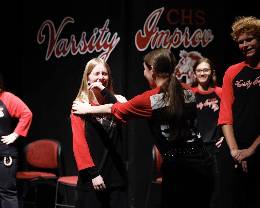 Students in black/red shirts "Improve" on stage laughing