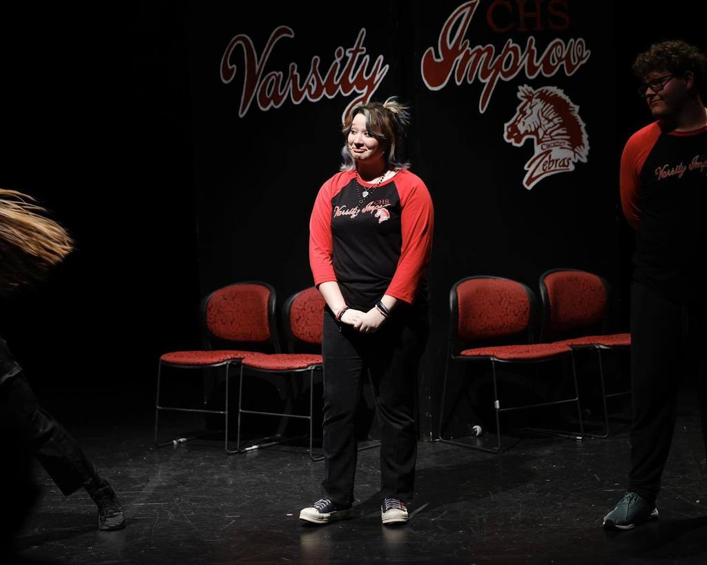 Students in black/red shirts "Improve" on stage smerking