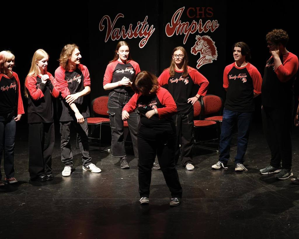 8 students in black/red shirts "Improve" on stage 