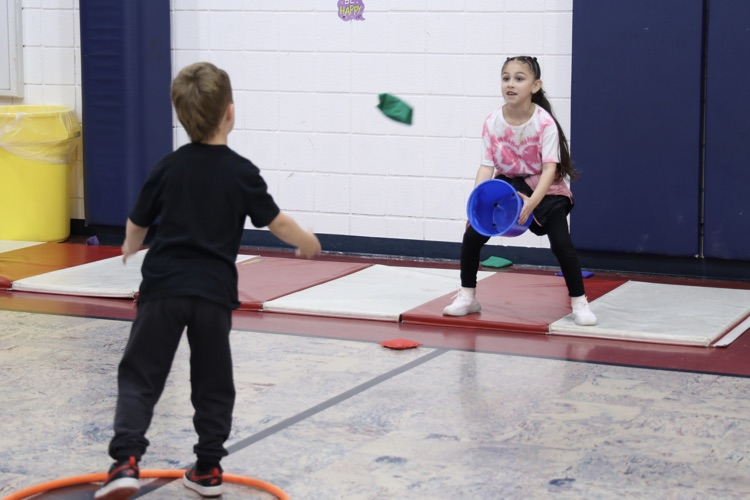 Little boy tossing a beanbag to a girl holding a bucket