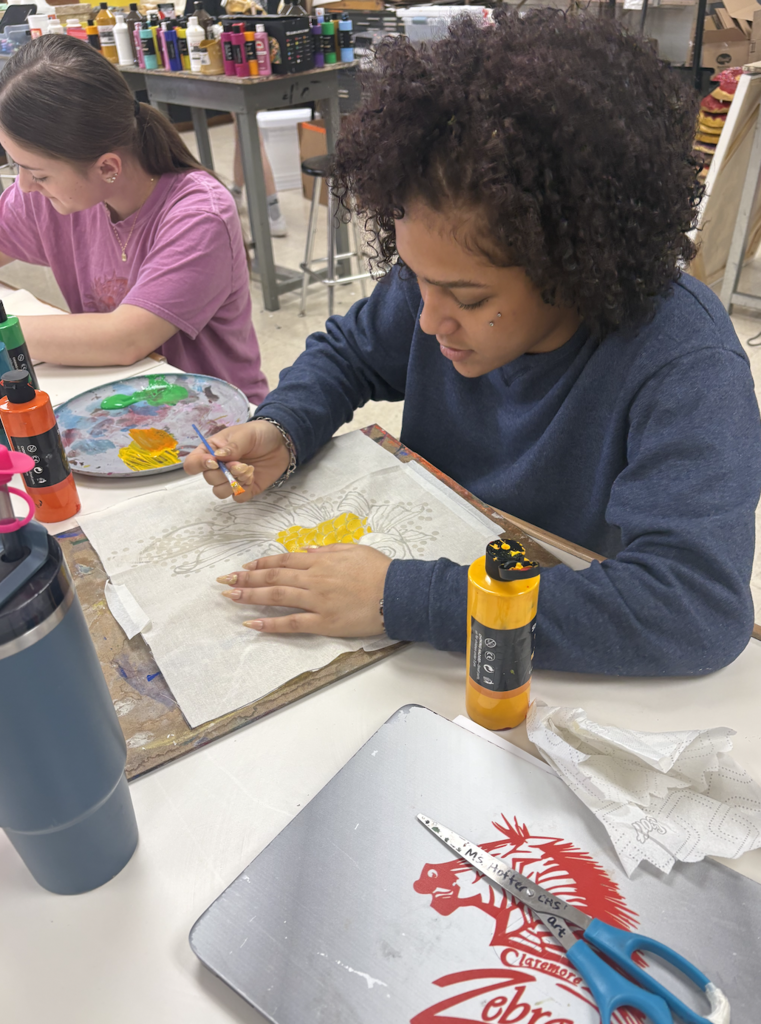 Students are discovering the exciting art of Batik! Batik is a fabric art technique where melted wax is applied to cloth to block out certain areas before dyeing. The wax is drawn on the fabric with a traditional tjanting tool, then the piece is hand painted. To reveal the final masterpiece, students remove the wax by ironing the fabric between sheets of newsprint and then washing away any remaining residue—unveiling bold contrasts, luminous color, and rich designs.