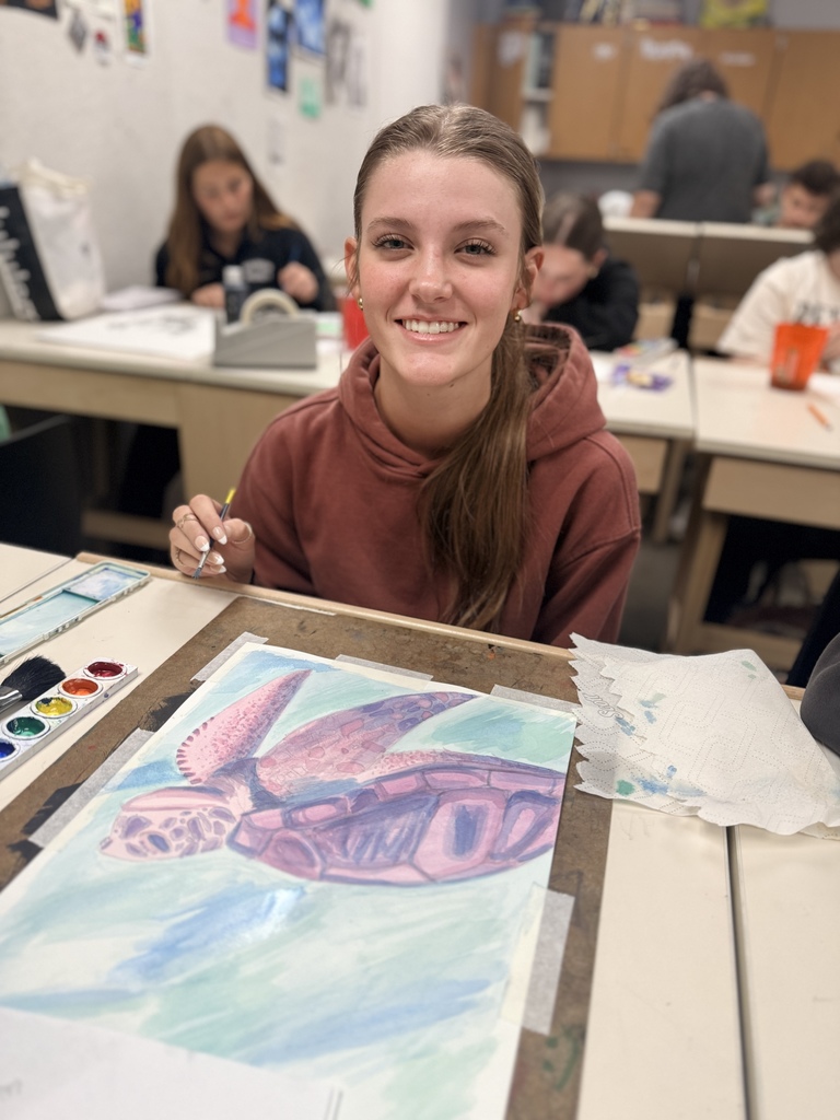 Student smiling while drawing a sea turtle in art class.