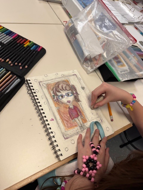 Student drawing a picture of another student in art using colored pencils 