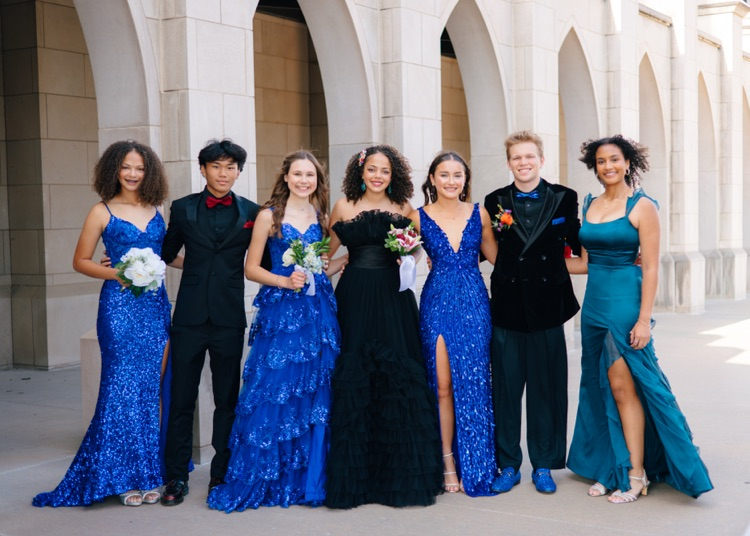 Group of students smiling for picture. Wearing prom attire. Blue and black suits and dresses 