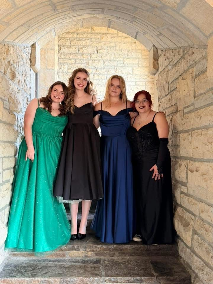 Group of four girls smiling for picture. Wearing prom dresses
