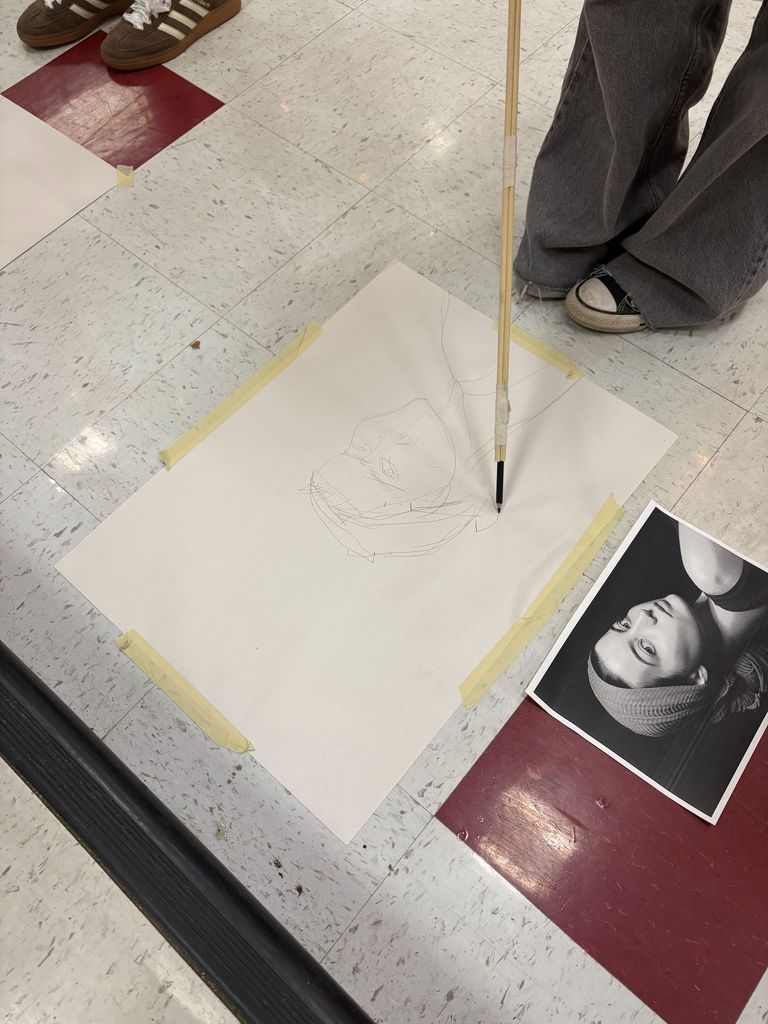 Student using a pen and a long stick to draw a picture during an art challenge