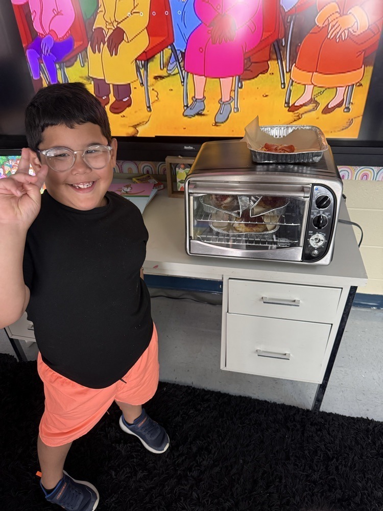 Elementary student next to their homemade pizza.