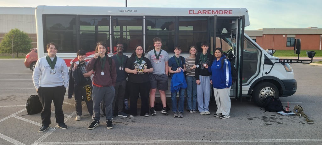 kids standing outside a buss with the medals they won