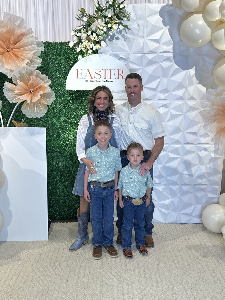 Mrs. Baldwin with husband and two kids smiling in front of an Easter set up