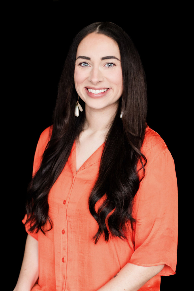 Shyla in orange shirt in front of black background smiling