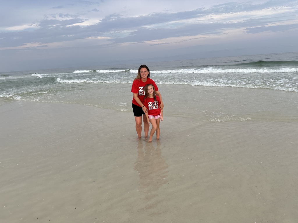 Rebecca and Natalie Stanart stand together in the shallow water at Pensacola Beach with waves and the ocean behind them.