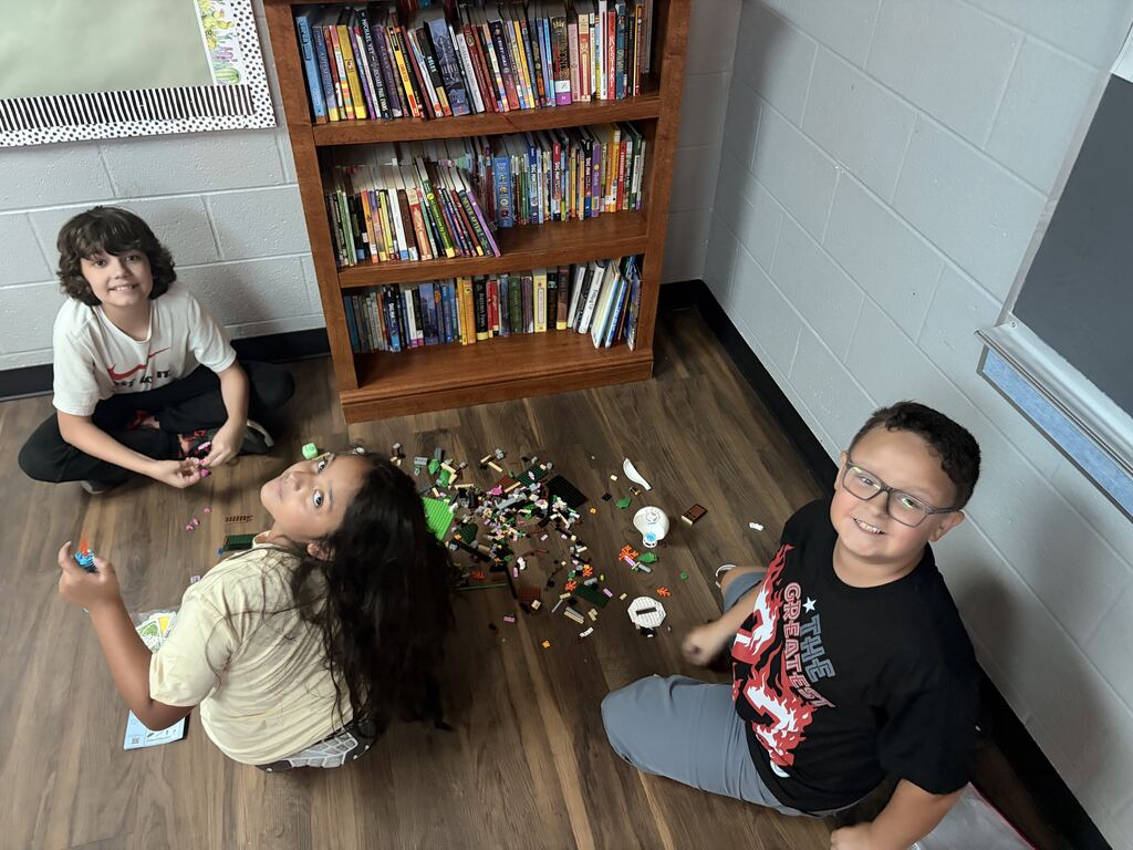 3 students looking at the camera, sitting in the floor, smiling