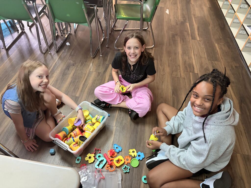 3 female students sitting in the floor with play-doh, smiling