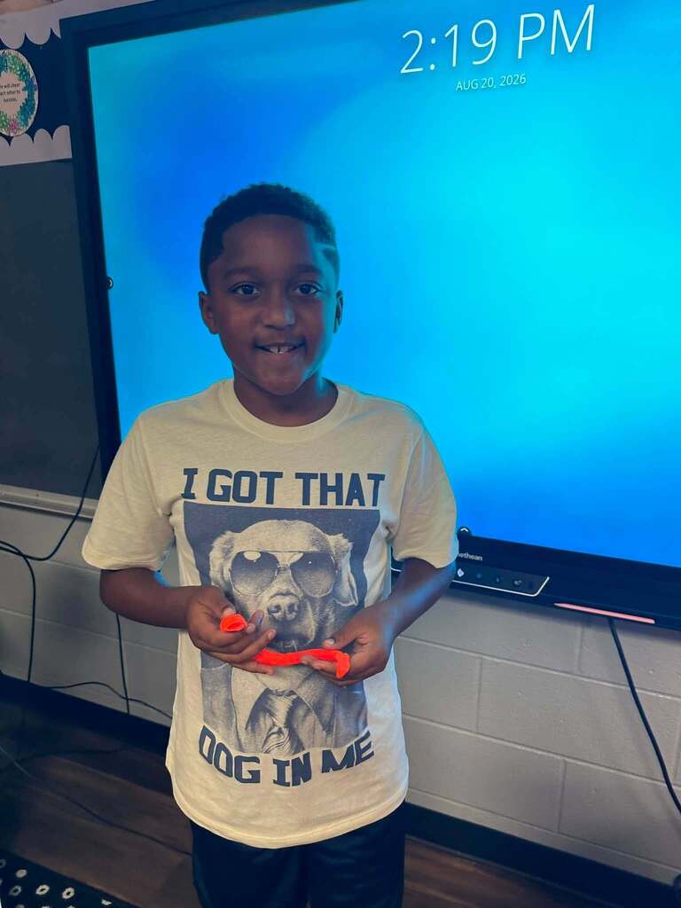 student holding playdoh that is orange - smiling