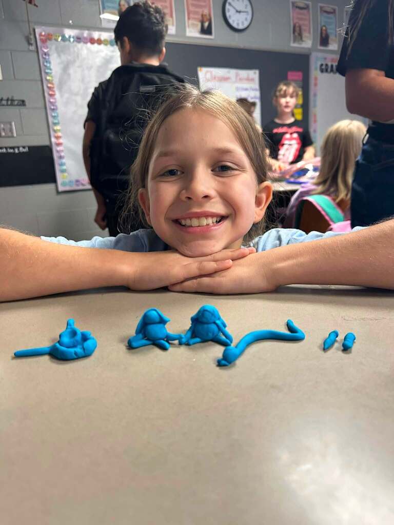 student showing what she made with blue playdoh, smiling
