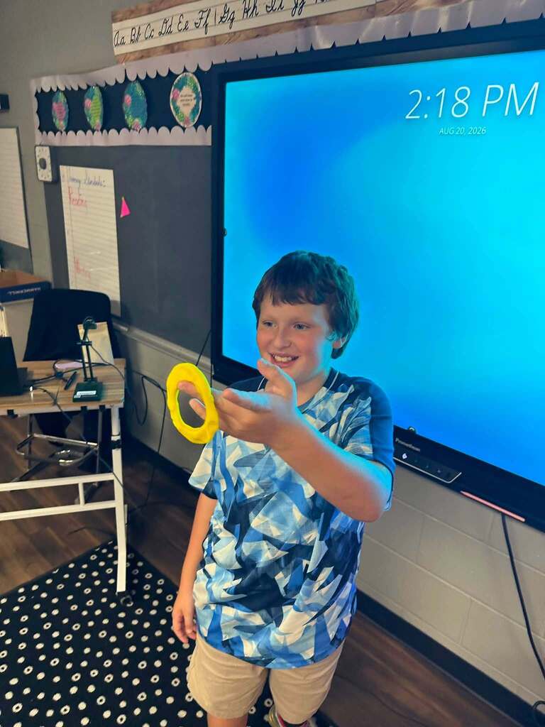 student holding yellow playdoh in the shape of an o, smiling