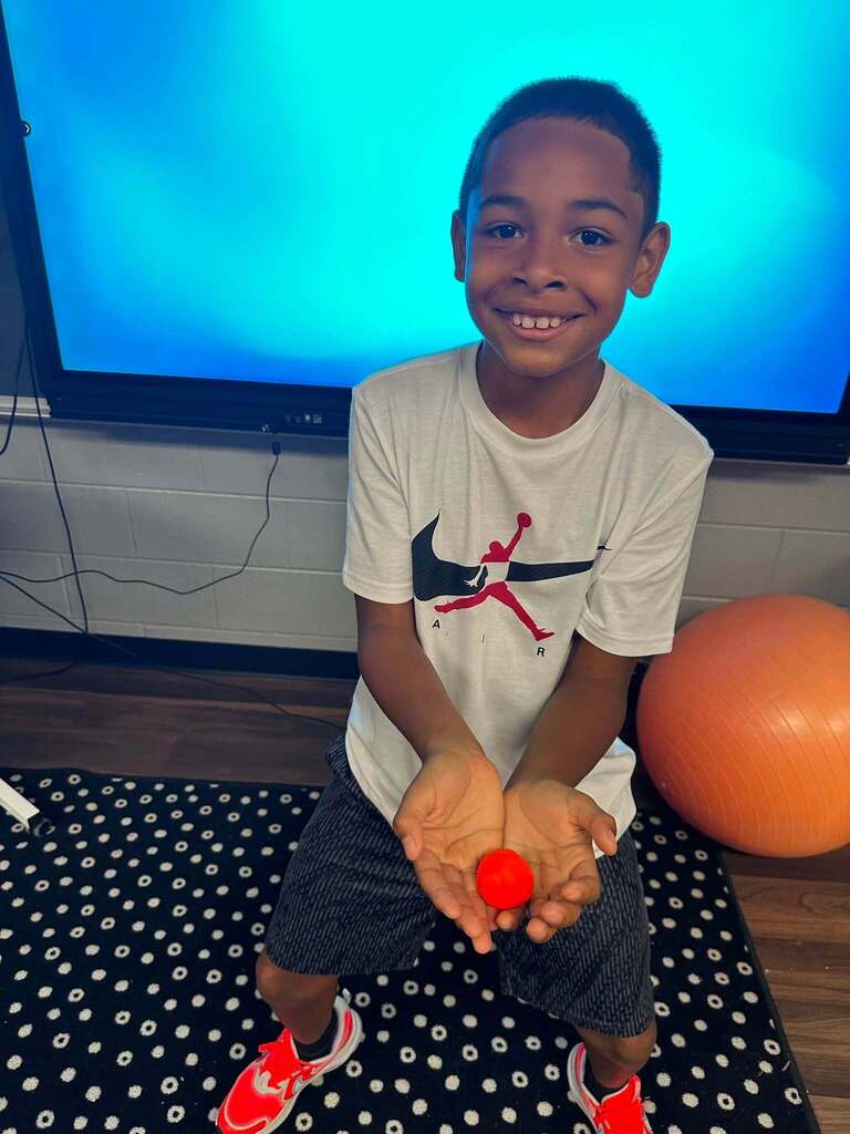 student holding red playdoh smiling