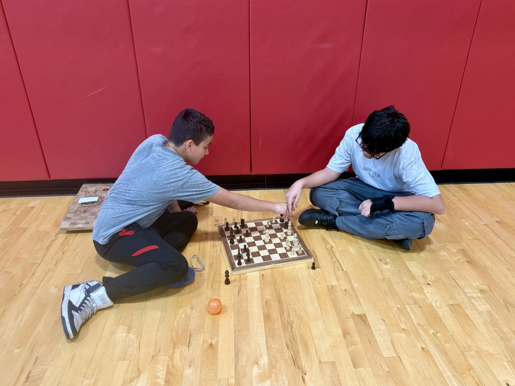 students sitting on gym floor playing chess together