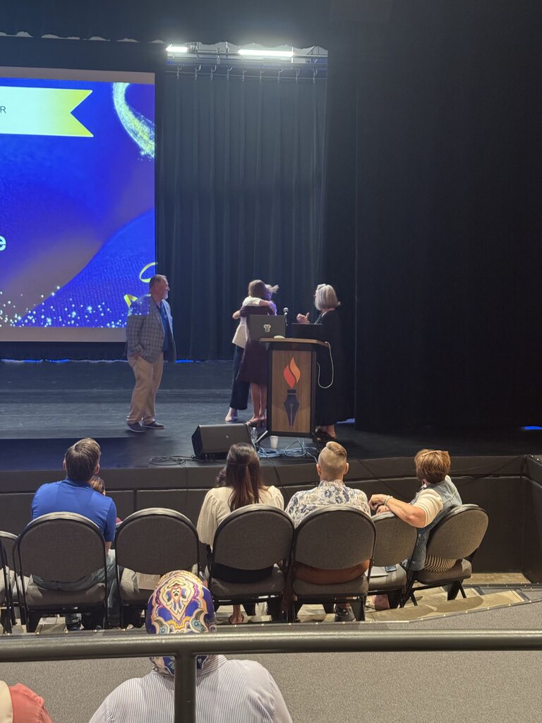 teacher on stage hugging other members after being recognized 