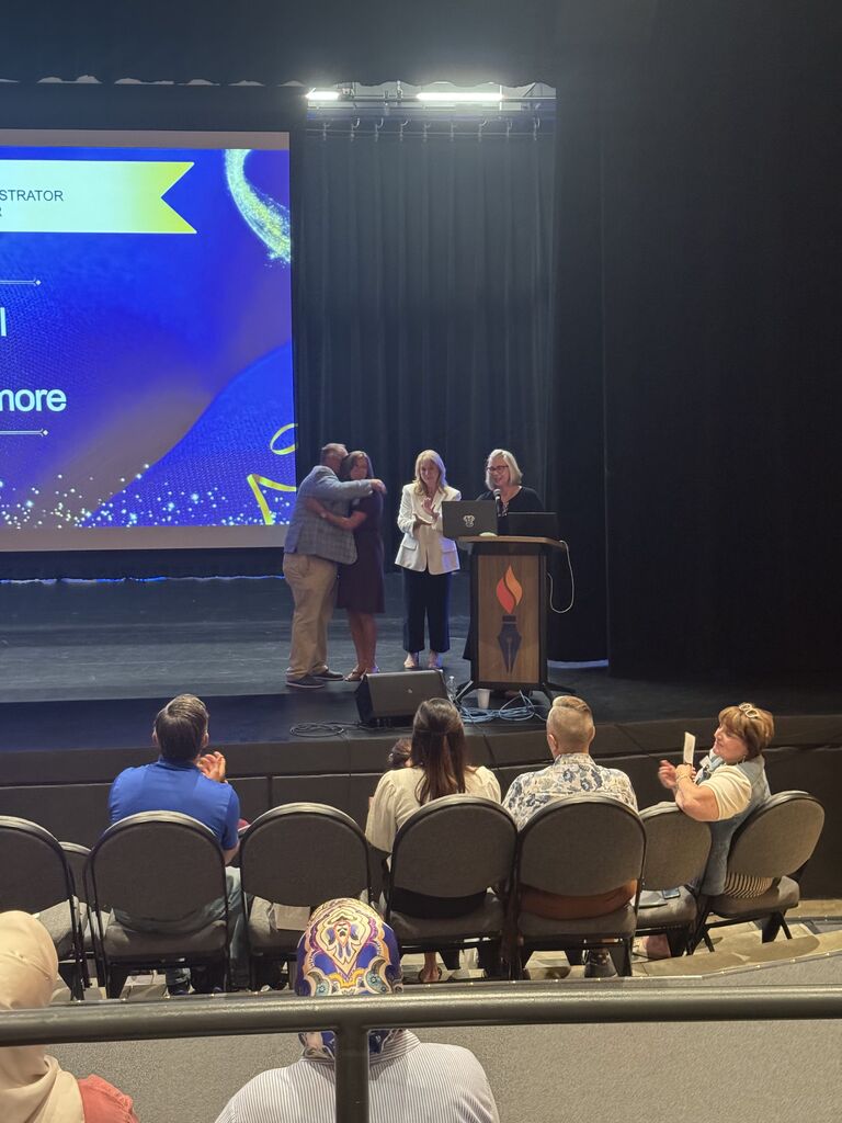 teacher on stage hugging other members after being recognized