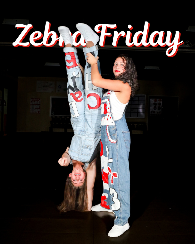 Two students in painted overalls doing a one hand handstand pose.