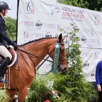 Student equestrian rider displaying an award ribbon with her horse.