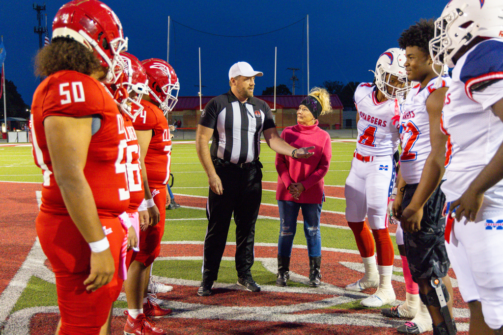 Football players gather at midfield for coin-toss with a Pink Out honoree.