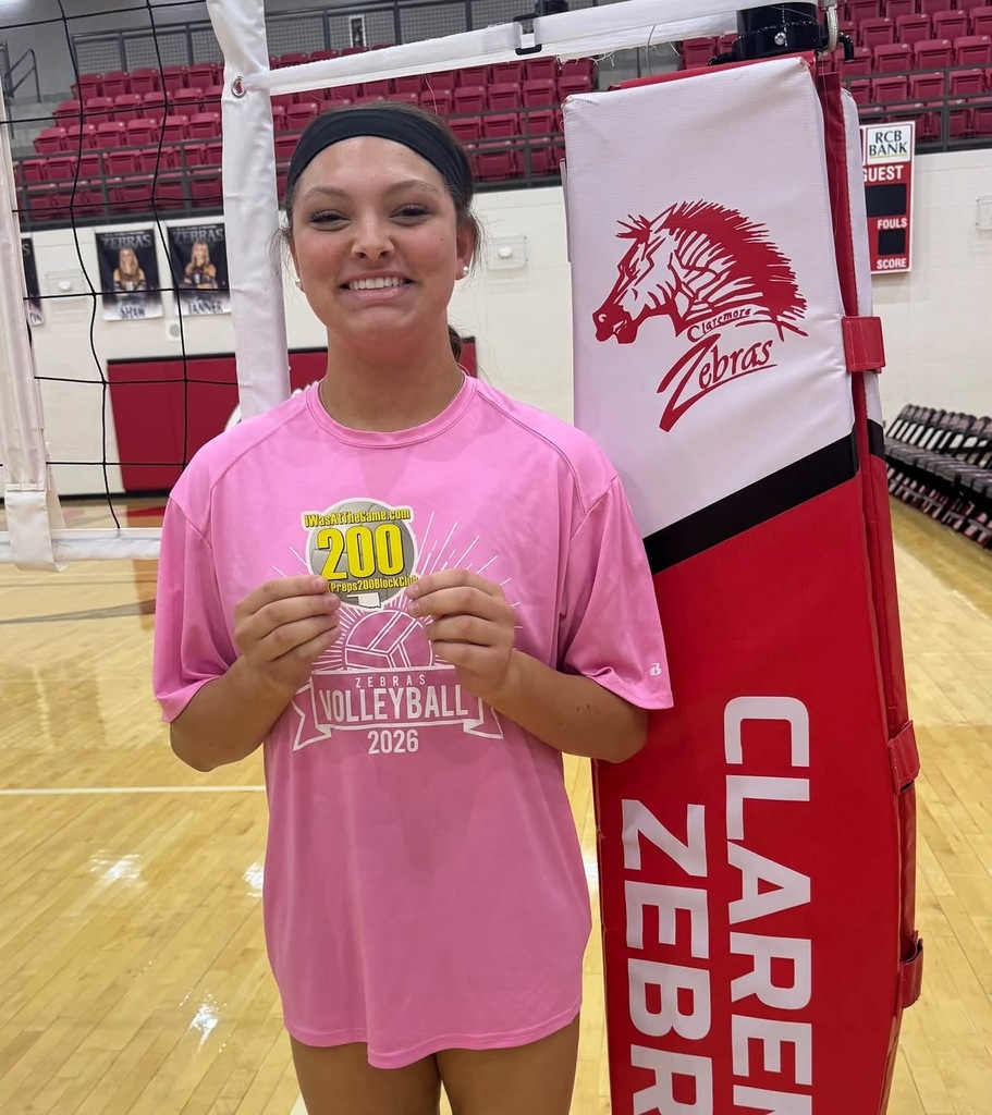 Addison Doyle holds her 200 career blocks milestone sticker beside the volleyball net.