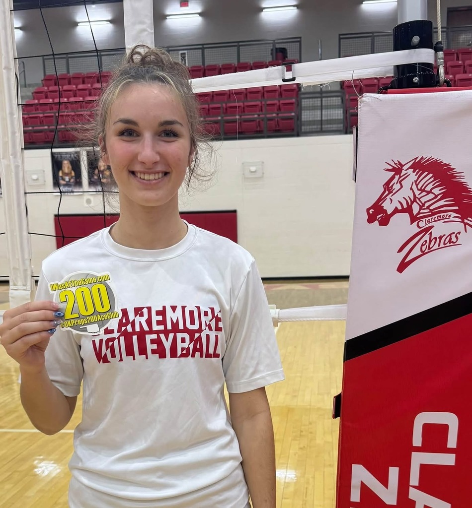 Grace Baughman holds her 200 career aces milestone sticker beside the volleyball net.