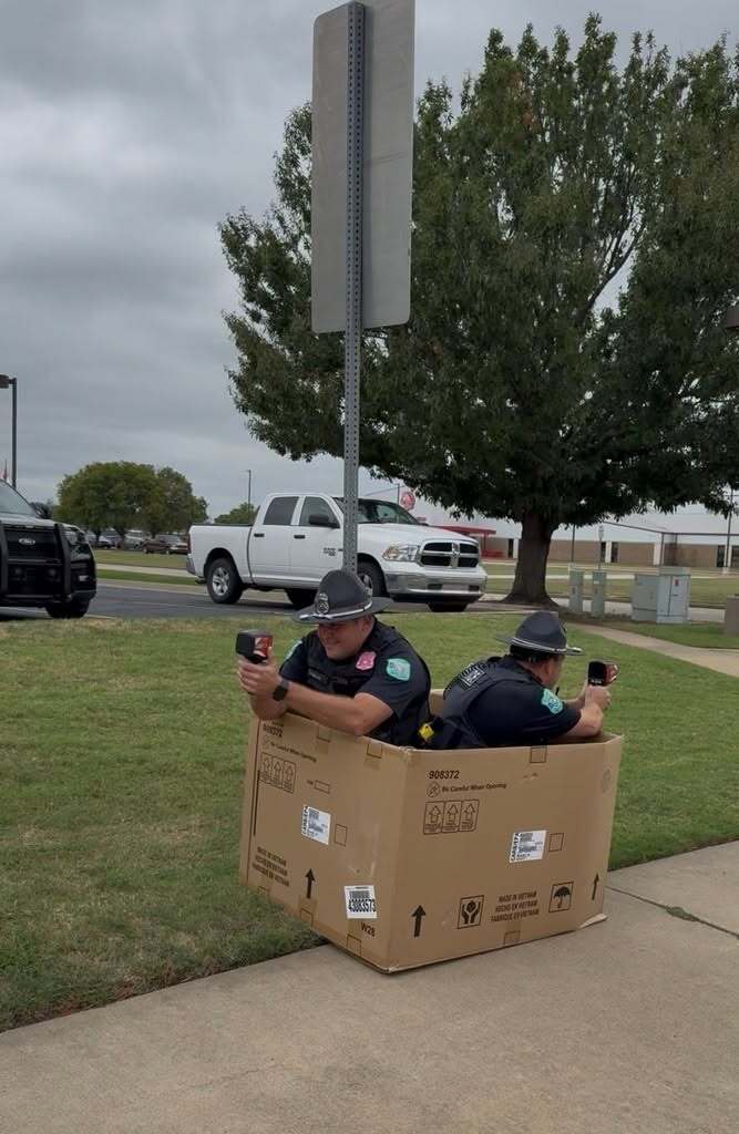 Two Claremore SROs sit inside a large cardboard box while monitoring the school zone.