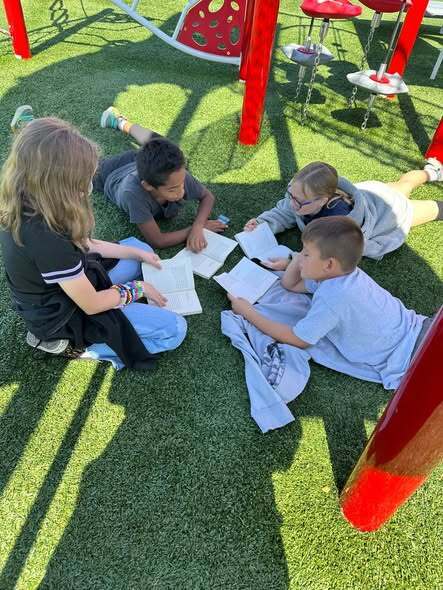 students sitting on grass reading books together