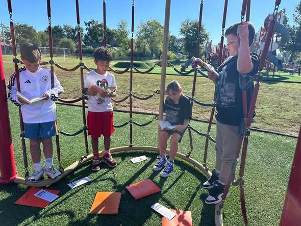 students sitting nd standing on playground equipment reading books together