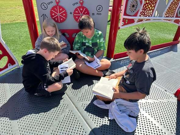 students sitting on playground equipment reading books together