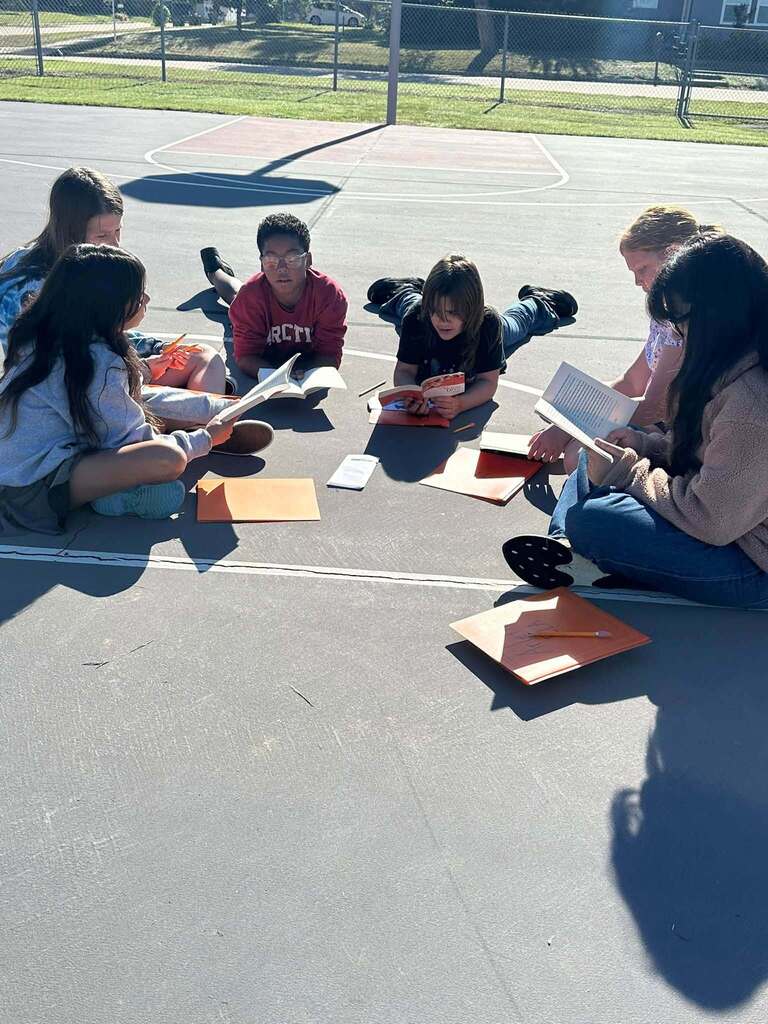 students sitting on basketball court reading books together