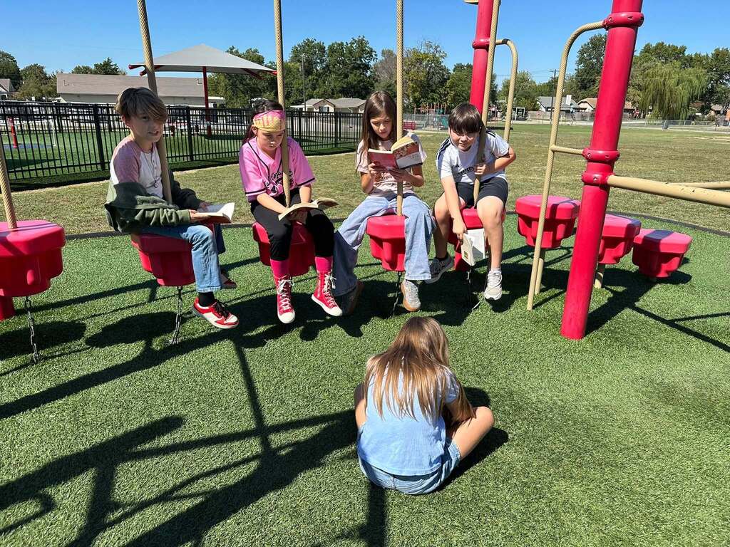 students sitting on playground equipment reading books together
