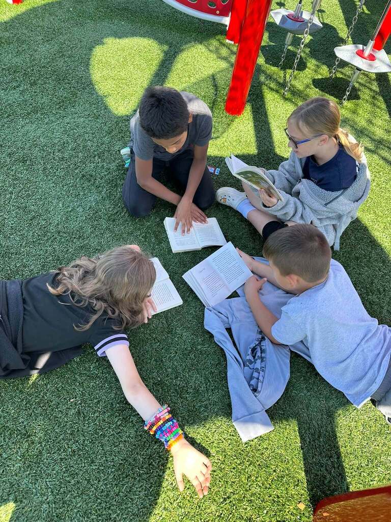 students sitting on grass reading books together