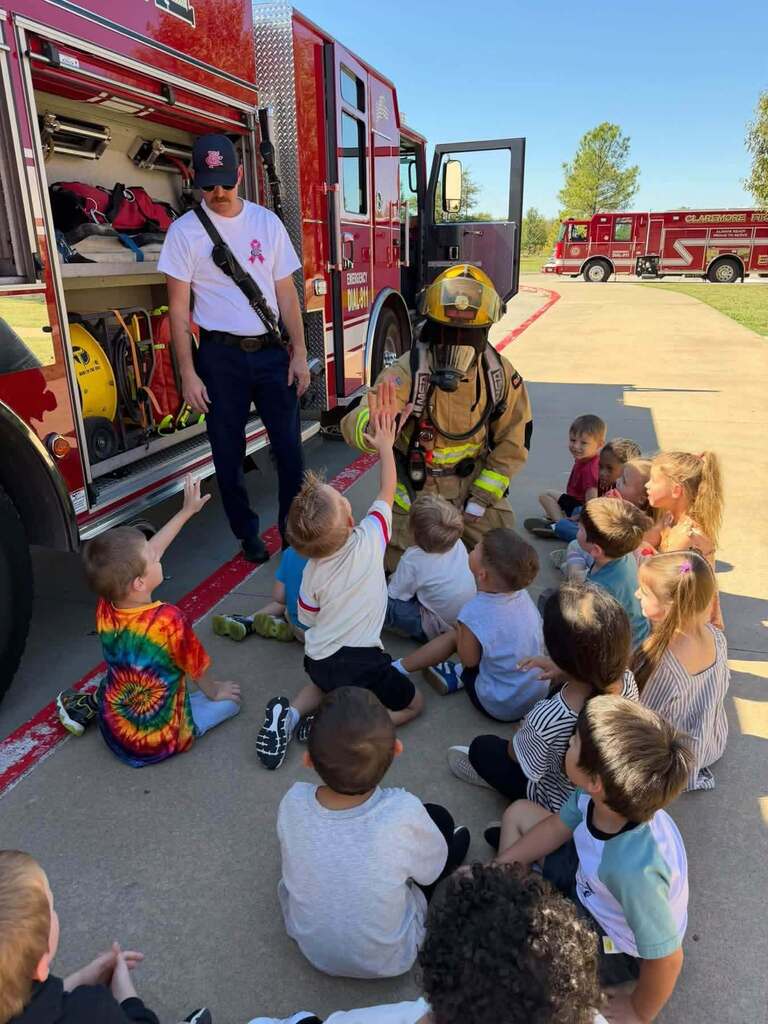 Student high-fives a firefighter in full gear while classmates watch.