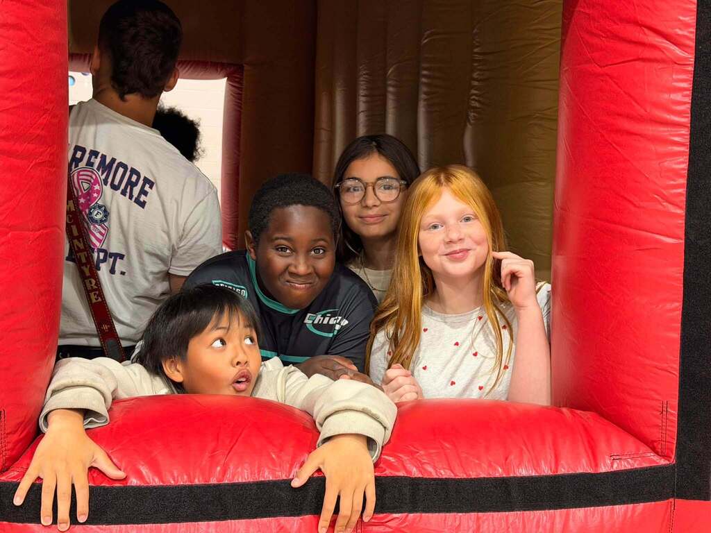 Four students smile through the window of the inflatable fire safety house.