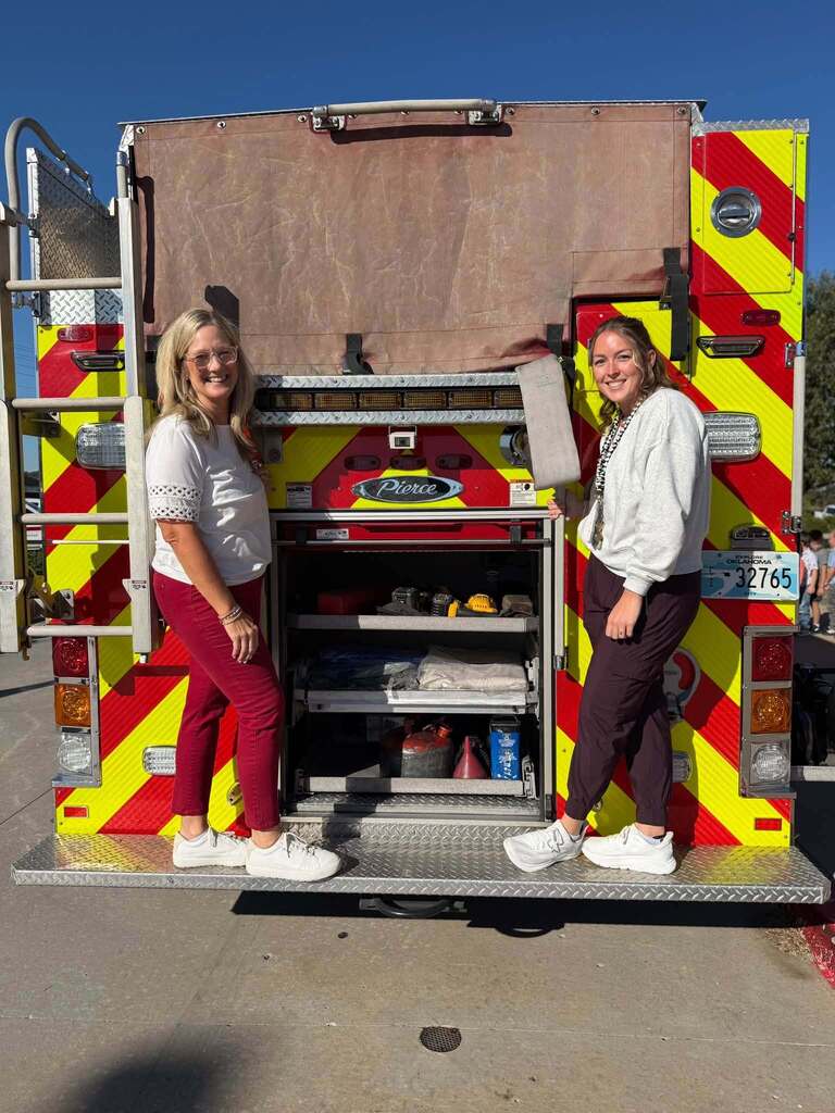 Two staff members pose at the back of a fire truck.