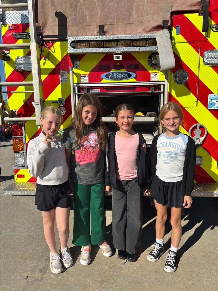 Four students smile in front of a fire truck.