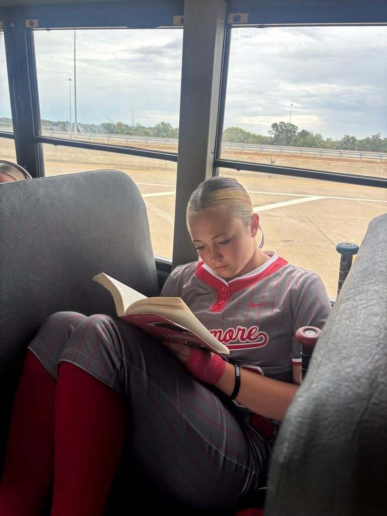 Lady Zebras softball player reading a book on the bus while traveling with her team.