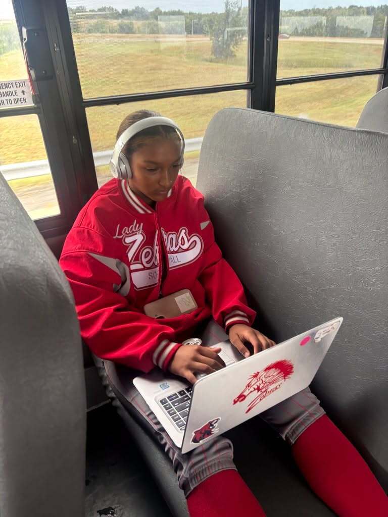 Lady Zebras softball player wearing headphones and working on a laptop during a bus ride.