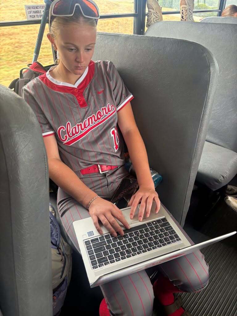 Lady Zebras softball player in uniform completing schoolwork on a laptop while riding the bus.