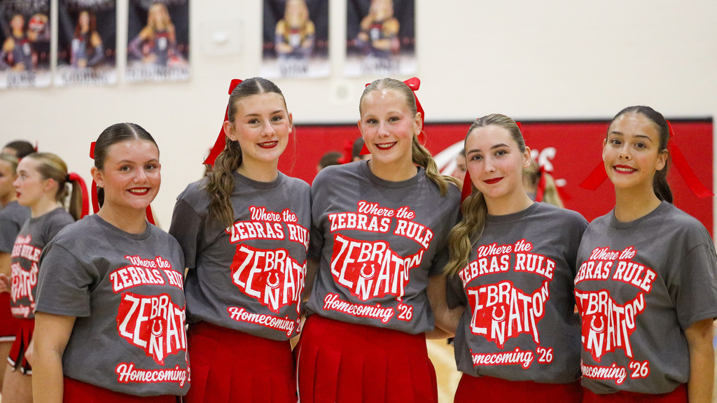 Five CHS dance team members pose in matching gray Homecoming shirts and red skirts.